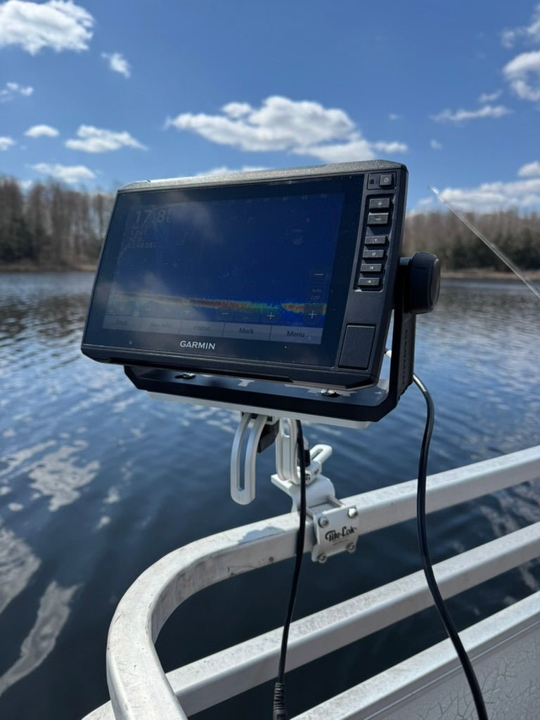 A Garmin fish finder mounted on a boat railing, with water and a blue sky in the background.